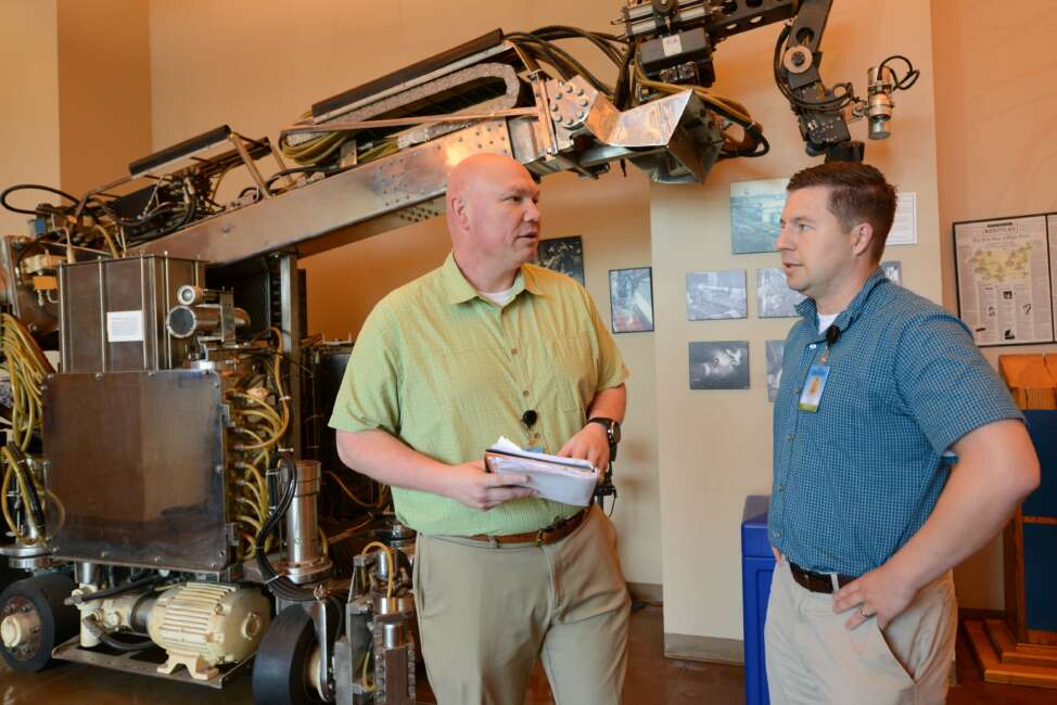 Doug Matty (left), director of AI capabilities at the Army’s AI Task Force, discusses an AI app for talent management being developed by Maj. Kevin Goulding (right). Behind them in the lobby of the National Robotics Engineering Center .