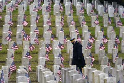 Retired U.S.Army veteran Bill MacCully walks among flag-covered graves in the Veterans Cemetery of Evergreen Washelli Memorial Park on Veterans Day, Wednesday, Nov. 11, 2020, in Seattle. (AP Photo/Elaine Thompson)