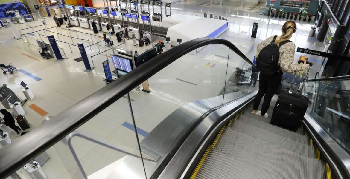 A traveler rides an escalator with her luggage as she arrives at the nearly empty JetBlue terminal at Logan Airport, Friday Nov. 20, 2020, in Boston. With the coronavirus surging out of control, the nation's top public health agency pleaded with Americans not to travel for Thanksgiving and not to spend the holiday with people from outside their household. (AP Photo/Michael Dwyer)