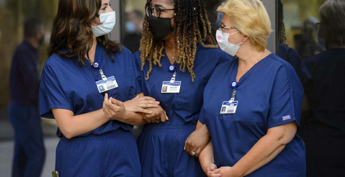 Shereyah Barbera, Annice Sterling, and Magdelena Litwinczuk, ICU nurses from Northwell Health, a New York hospital chain, who will support ICU teams at Intermountain Healthcare in Utah, link arms at a news conference in Murray, Utah on Tuesday, Aug. 4, 2020. (Trent Nelson/The Salt Lake Tribune via AP)