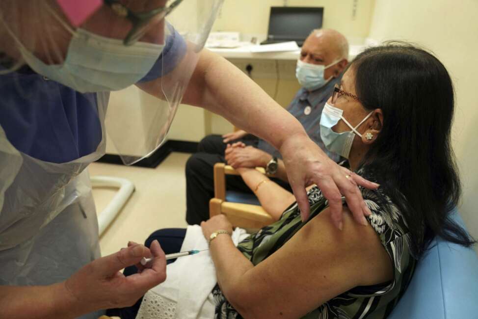 CORRECTS NAME  Ranjan Shukla, accompanied by her husband Dr Hari Shukla, receives the Pfizer-BioNTech COVID-19 vaccine at the Royal Victoria Infirmary in Newcastle, England, Tuesday Dec. 8, 2020. The United Kingdom, one of the countries hardest hit by the coronavirus, is beginning its vaccination campaign, a key step toward eventually ending the pandemic. (Owen Humphreys/Pool via AP)