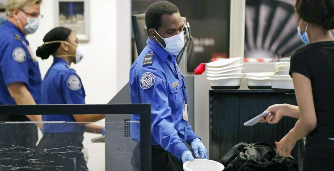 FILE - In this May 18, 2020 file photo TSA officers wear protective masks at a security screening area at Seattle-Tacoma International Airport in SeaTac, Wash. Federal safety officials are investigating people who took part in last week's riot at the U.S. Capitol to decide whether they belong on the federal no-fly list. The move is one of several that officials outlined Friday, Jan. 15, 2021. (AP Photo/Elaine Thompson, File)