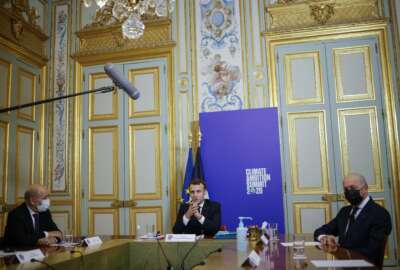 FILE - In this Dec. 12, 2020, file photo, French President Emmanuel Macron, center flanked by French Foreign Minister Jean-Yves Le Drian, left, and President of the French Constitutional Council Laurent Fabius, right, speaks during the Climate Ambition Summit 2020 video conference at the Elysee Palace in Paris. World leaders are applauding Friday's formal return of the U.S. to the mostly voluntary 2015 agreement, saying it is symbolic and important. They say they expect the United States to show leadership in the fight against warming by setting strong targets for carbon pollution cuts by 2030.(Yoan Valat, Pool via AP)