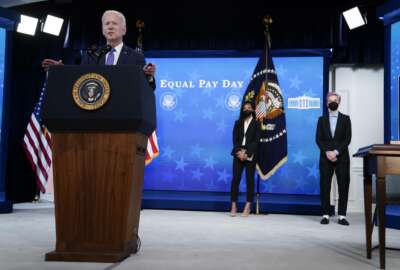 United States Soccer Women's National Team members Margaret Purce, center, and Megan Rapinoe, right, look on as President Joe Biden speaks during an event to mark Equal Pay Day in the South Court Auditorium in the Eisenhower Executive Office Building on the White House Campus Wednesday, March 24, 2021, in Washington. (AP Photo/Evan Vucci)