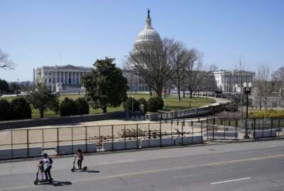 People ride scooters past an inner perimeter of security fencing on Capitol Hill in Washington, Sunday, March 21, 2021, after portions of an outer perimeter of fencing were removed overnight to allow public access. (AP Photo/Patrick Semansky)
