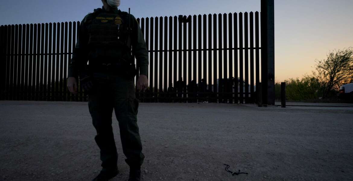 A U.S. Customs and Border Protection agent looks on near a gate on the U.S.-Mexico border wall as agents take migrants into custody, Sunday, March 21, 2021, in Abram-Perezville, Texas. The fate of thousands of migrant families who have recently arrived at the Mexico border is being decided by a mysterious new system under President Joe Biden. U.S. authorities are releasing migrants with “acute vulnerabilities” and allowing them to pursue asylum. But it’s not clear why some are considered vulnerable and not others. (AP Photo/Julio Cortez)
