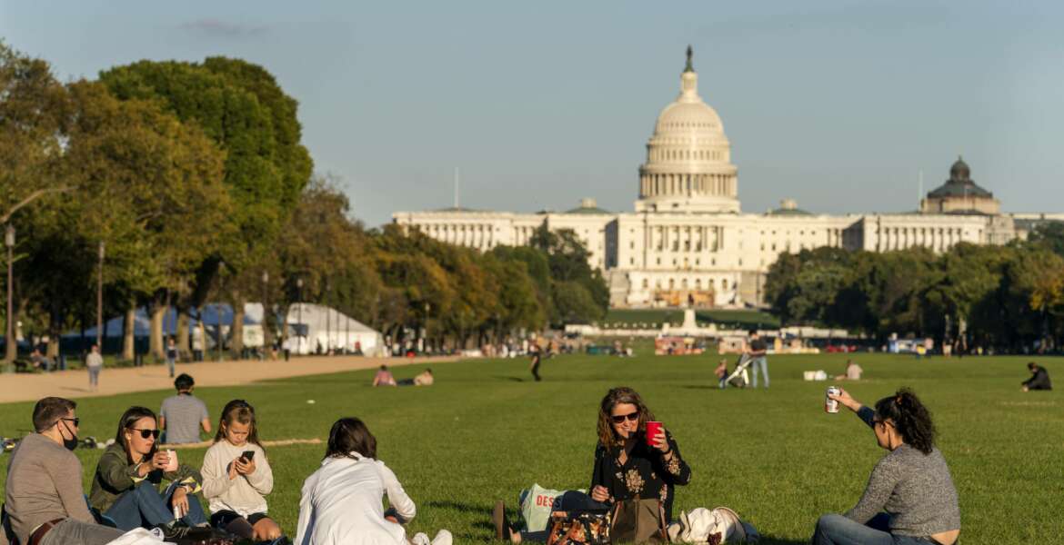 FILE - In this Oct. 8, 2020, file photo with the Capitol in the background, two women toast in the air from afar while enjoying a warm fall afternoon as the sun begins to set on the National Mall in Washington. Officials in the nation's capital are questioning the results of the 2020 census, which show a large boost in population but not as high as they had expected. (AP Photo/Jacquelyn Martin, File)