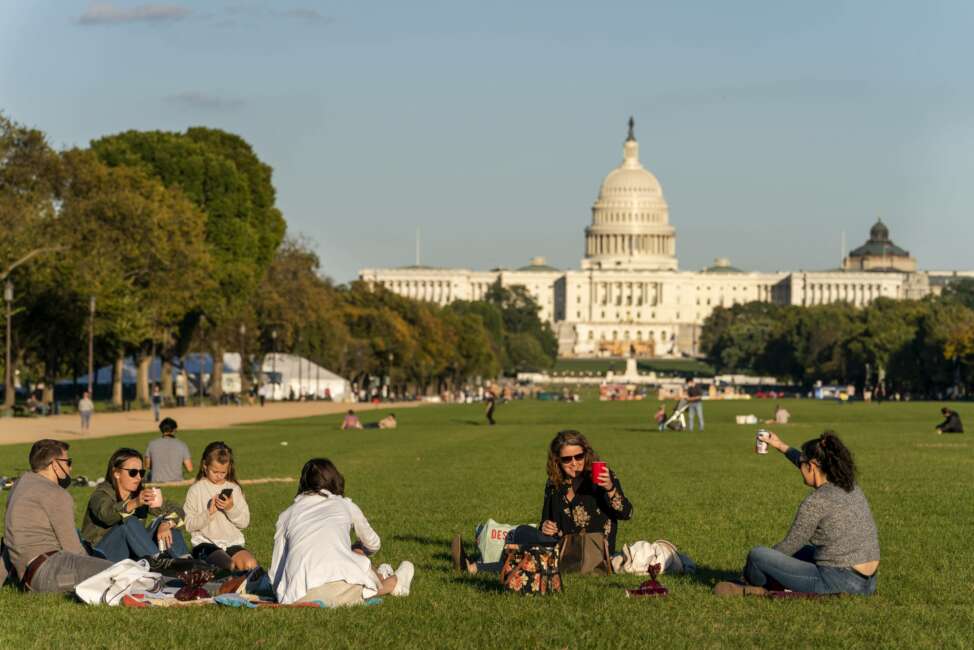 FILE - In this Oct. 8, 2020, file photo with the Capitol in the background, two women toast in the air from afar while enjoying a warm fall afternoon as the sun begins to set on the National Mall in Washington. Officials in the nation's capital are questioning the results of the 2020 census, which show a large boost in population but not as high as they had expected. (AP Photo/Jacquelyn Martin, File)