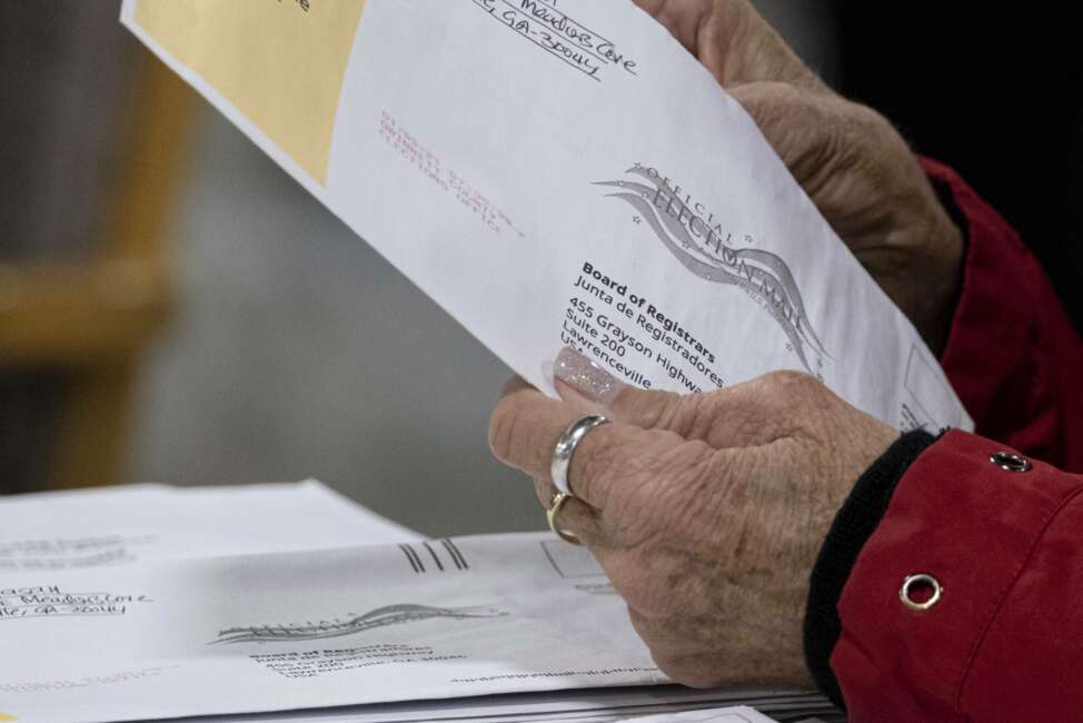 FILE - In this Jan. 6, 2021 file photo, workers at the Gwinnett County Georgia elections headquarters process absentee ballots for Georgia's Senate runoff election in Lawrenceville, Ga.  When voters in Florida and Georgia request mailed ballots next year, they will have to make sure they do one more thing before sending it in: provide proof of identification.  (AP Photo/Ben Gray, File)