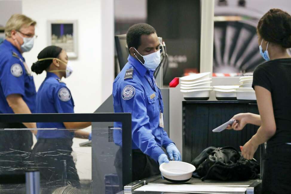 FILE - In this May 18, 2020, file photo, Transportation Security Administration officers wear protective masks at a security screening area at Seattle-Tacoma International Airport in SeaTac, Wash. The Biden administration says it is moving to increase the pay and union rights for security screeners at the nation’s airports. The Department of Homeland Security directed the acting head of the TSA to come up with a plan within 90 days to raise the pay of the screeners and expand their rights to collective bargaining.  (AP Photo/Elaine Thompson, File)