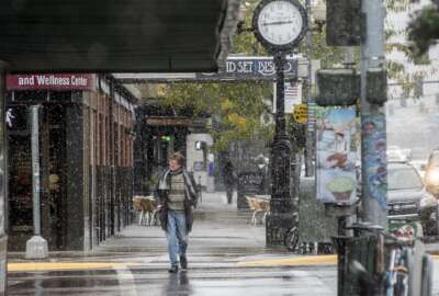 FILE - In this Sept. 29, 2019 file photo, a pedestrian crosses Front Street under snowfall in Missoula, Mont.  Lawmakers are trying to stop 144 cities across the U.S. from losing their designations as “metropolitan areas” because the federal government is upgrading the standard from a minimum of 50,000 residents in its core to a minimum of 100,000 people. Missoula is among those at risk of losing the designation.   (Ben Allan Smith/The Missoulian via AP, File)