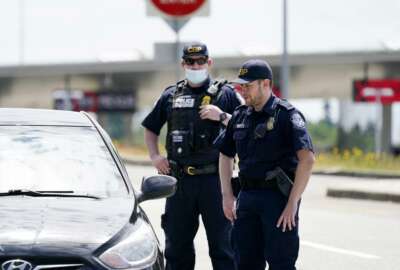 Customs and Border Protection officers direct a driver on who missed the last turn before entry into Canada on how to turn around at the Peace Arch border crossing into the U.S., Tuesday, June 8, 2021, in Blaine, Wash. The border has been closed to nonessential travel since March 2020. (AP Photo/Elaine Thompson)