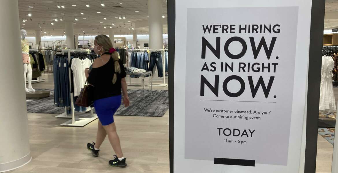 A customer walks behind a sign at a Nordstrom store seeking employees, Friday, May 21, 2021, in Coral Gables, Fla.  The number of Americans seeking unemployment benefits dropped last week to 406,000, a new pandemic low and more evidence that the job market is strengthening as the virus wanes and economy further reopens. (AP Photo/Marta Lavandier)