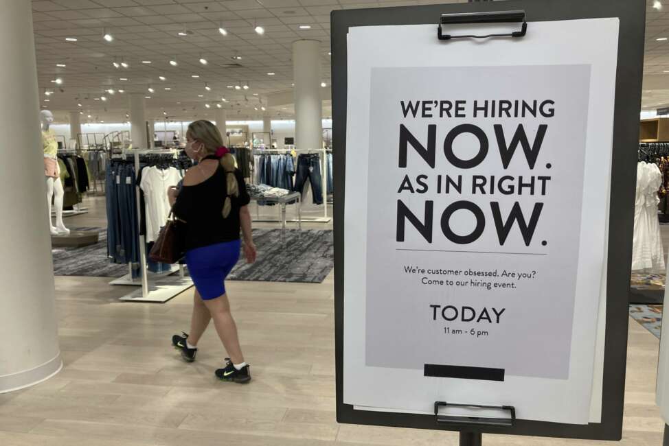 A customer walks behind a sign at a Nordstrom store seeking employees, Friday, May 21, 2021, in Coral Gables, Fla.  The number of Americans seeking unemployment benefits dropped last week to 406,000, a new pandemic low and more evidence that the job market is strengthening as the virus wanes and economy further reopens. (AP Photo/Marta Lavandier)