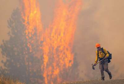 After walking down a gravel road to do recon on a fire cresting into the trees, a wildland firefighter grimaces as he walks back to his crew on Thursday, Aug. 12, 2021, at the Bedrock Fire north of Lenore, Idaho. Lenore is about 30 miles east of Lewiston, Idaho. (Pete Caster/Lewiston Tribune via AP)