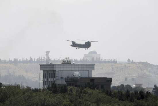 FILE - In this Sunday, Aug. 15, 2021 file photo, a U.S. Chinook helicopter flies near the U.S. Embassy in Kabul, Afghanistan, as diplomatic vehicles leave the compound amid the Taliban advance on the capital. (AP Photo/Rahmat Gul)
