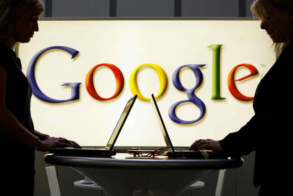 FILE - In this April 17, 2007, file photo, exhibitors work on laptop computers in front of an illuminated sign of the Google logo at the industrial fair Hannover Messe in Hanover, Germany. Google has announced that it is investing $1.2 billion by 2030 to expand its cloud computing infrastructure in Germany and to increase the use of renewable energy. The Internet giant said Tuesday that it plans to add new cloud computing centers in the Berlin region and in Hanau, a town near Frankfurt.  (AP Photo/Jens Meyer, File)