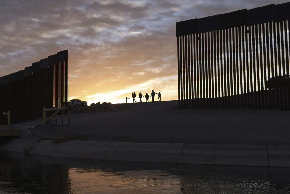 FILE - In this June 10, 2021 file photo, a pair of migrant families from Brazil pass through a gap in the border wall to reach the United States after crossing from Mexico to Yuma, Ariz., to seek asylum. As the delta variant fuels an increase of COVID-19 cases in the U.S., some of President Joe Biden's critics blame the surge on his border policies, which allow some migrants to enter the country to apply for asylum. (AP Photo/Eugene Garcia, File)