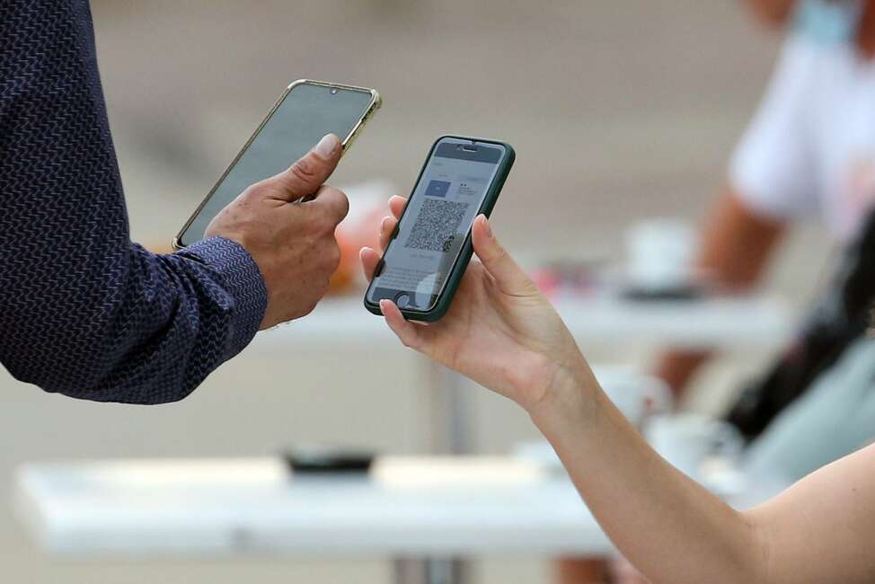 A waiter checks clients' health passes at a restaurant in Ascain, southwestern France, Wednesday, Aug. 11, 2021. People in France are now required to show a QR code proving they have a special virus pass to enjoy restaurants and cafes or travel across the country. (AP Photo/Bob Edme)