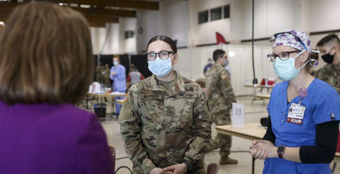FILE - In this Wednesday, Jan. 13, 2021, file photo, Oregon Gov. Kate Brown, left back to camera, talks with a National Guard member and registered nurse during a visit to the Marion County and Salem Health vaccination clinic at the Oregon State Fairgrounds in Salem, Ore. Brown said Friday, Aug. 13, she will send up to 1,500 National Guard troops to hospitals around the state to assist healthcare workers who are being pushed to the brink by a surge of COVID-19 cases driven by the Delta variant. (Abigail Dollins/Statesman-Journal via AP, Pool, File)
