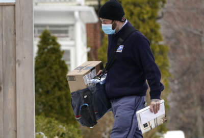 Postal carrier Josiah Morse delivers mail and packages, Wednesday, Feb. 3, 2021, in Portland, Maine. The U.S. Postal Service's stretch of challenges didn't end with the November general election and tens of millions of mail-in votes. The pandemic-depleted workforce fell further into a hole during the holiday rush, leading to long hours and a mountain of delayed mail. (AP Photo/Robert F. Bukaty)