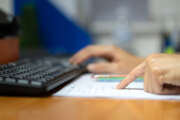 Close-up action of at person's finger in pointing to correct the data on paper with blurred background of the another hand is typing keyword to input data in computer. Business working photo.