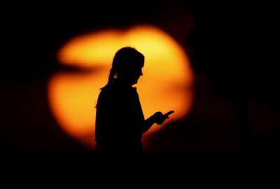 FILE - In this Monday, June 29, 2020, file photo, a woman looks at her phone in a park as the sun sets in Kansas City, Mo. On Wednesday, Sept. 15, 2021, a divided federal appeals court upheld the dismissal of an ACLU lawsuit challenging a portion of the National Security Agency's warrantless surveillance of Americans' international email and phone communications. (AP Photo/Charlie Riedel, File)
