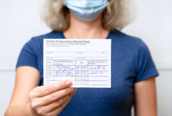 Moscow - Sep 12, 2021: Vaccinated young woman showing COVID-19 Vaccination Record Card, healthy person in mask after getting corona virus vaccine. Coronavirus vaccine shot and immunization mandate.