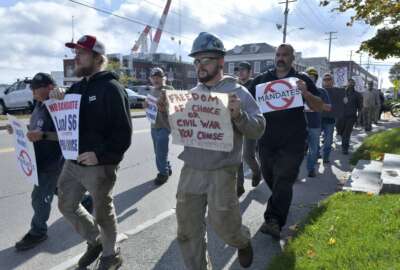 Justin Paetow, center, a tin shop worker at Bath Iron Works, takes part in a demonstration against COVID-19 vaccine mandate outside the shipyard on Friday, Oct. 22, 2021, in Bath, Maine. Some American workers are making the painful decision to quit their jobs and abandon cherished careers in defiance of what they consider intrusive vaccine mandates requiring all businesses with 100 or more workers be fully vaccinated against COVID-19. (AP Photo/Josh Reynolds)
