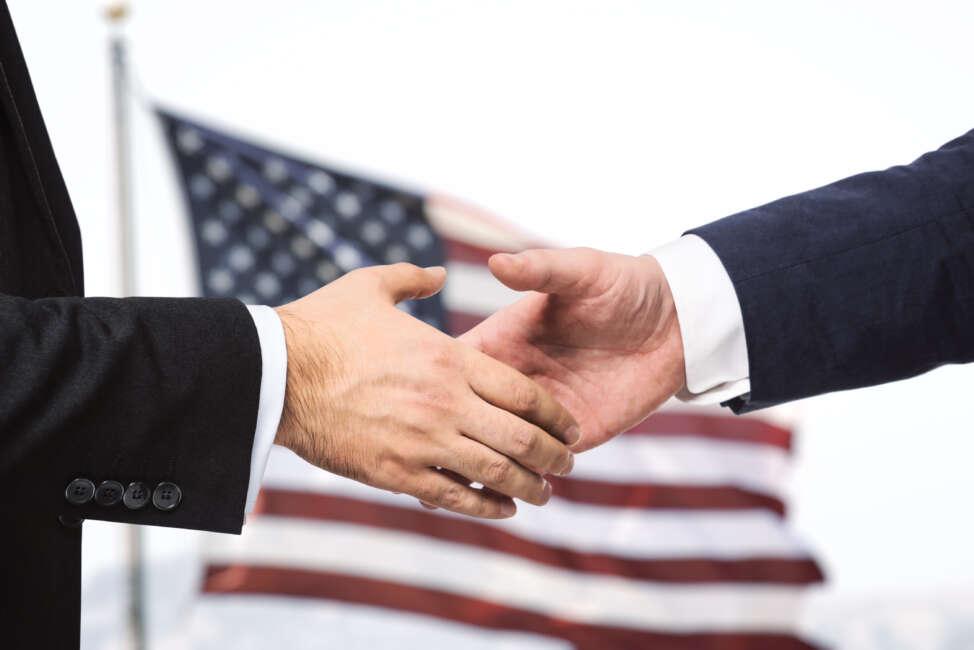 Two businessmen shake hands on a US flag backgrond, closeup