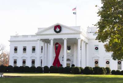 The North Portico of the White House is adorned with a huge red ribbon to commemorate the annual World AIDS Day, Wednesday, Dec. 1, 2021, in Washington. The Biden administration in its new HIV/AIDS strategy is calling racism 