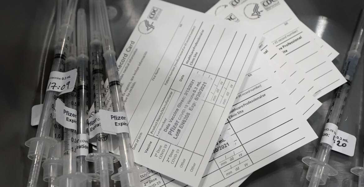 FILE - Syringes with doses of the Pfizer COVID-19 vaccine, are shown next to vaccination cards March 13, 2021, in Seattle. The District of Columbia government is imposing a series of COVID-19 vaccine mandates as it intensifies virus protocols in response to spiraling infection numbers and the march of the omicron variant. (AP Photo/Ted S. Warren, File)