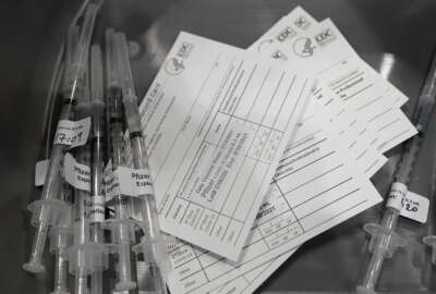 FILE - Syringes with doses of the Pfizer COVID-19 vaccine, are shown next to vaccination cards March 13, 2021, in Seattle. The District of Columbia government is imposing a series of COVID-19 vaccine mandates as it intensifies virus protocols in response to spiraling infection numbers and the march of the omicron variant. (AP Photo/Ted S. Warren, File)