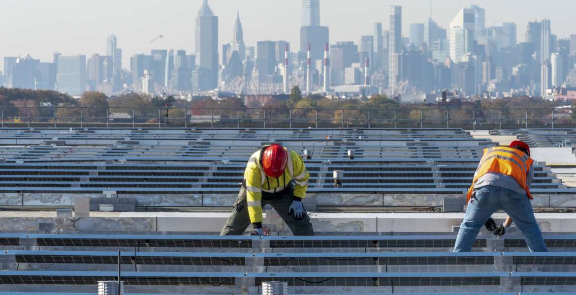 FILE - Framed by the Manhattan skyline electricians with IBEW Local 3 install solar panels on top of the Terminal B garage at LaGuardia Airport, Tuesday, Nov. 9, 2021, in the Queens borough of New York.  As climate change pushes states in the U.S. to dramatically cut their use of fossil fuels, many are coming to the conclusion that solar, wind and other renewable power sources won't be enough to keep the lights on. Nuclear power is emerging as an answer to fill the gap as states transition away from coal, oil and natural gas to reduce greenhouse gas emissions and stave off the worst effects of a warming planet. (AP Photo/Mary Altaffer, File)