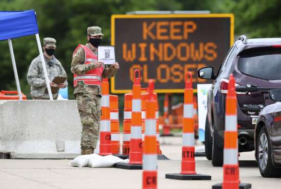 FILE - A National Guard member holds up a sign as vehicles enter a Test Iowa coronavirus testing site at the Kirkwood Community College Continuing Education Training Center in Cedar Rapids, Iowa, on May 28, 2020. State National Guard units are seeing dramatic re-enlistment rates, even as their troops juggle near constant duties with COVID-19, natural disasters and other military deployments. (Rebecca F. Miller/The Gazette via AP, File)