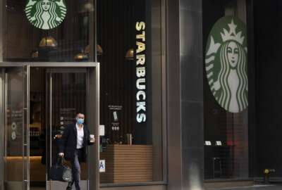 FILE - A man carries a beverage as he walks out of a Starbucks coffee shop, Tuesday, Jan. 19, 2021, in New York. Companies that would be affected by a Biden administration vaccine-or-testing requirement for workers remain on the sidelines while the Supreme Court considers whether the rule can be enforced. Since then, Starbucks has announced its own vaccine mandate saying in Dec. 2021, that all U.S. workers must be fully vaccinated by Feb. 9, 2022, or face a weekly COVID testing requirement. (AP Photo/Mark Lennihan, File)