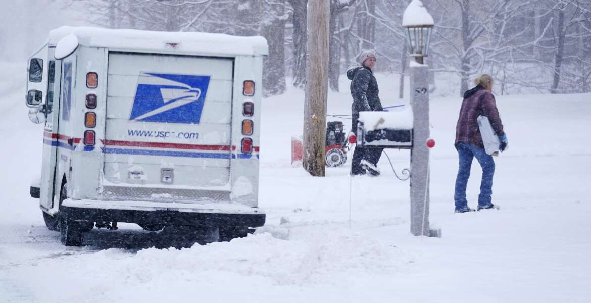 A US Postal Service carrier delivers a package during a snow storm Friday, Jan. 7, 2022, in East Derry, N.H. A winter storm is expected to drop about a half a foot of snow in the area. (AP Photo/Charles Krupa)