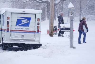 A US Postal Service carrier delivers a package during a snow storm Friday, Jan. 7, 2022, in East Derry, N.H. A winter storm is expected to drop about a half a foot of snow in the area. (AP Photo/Charles Krupa)