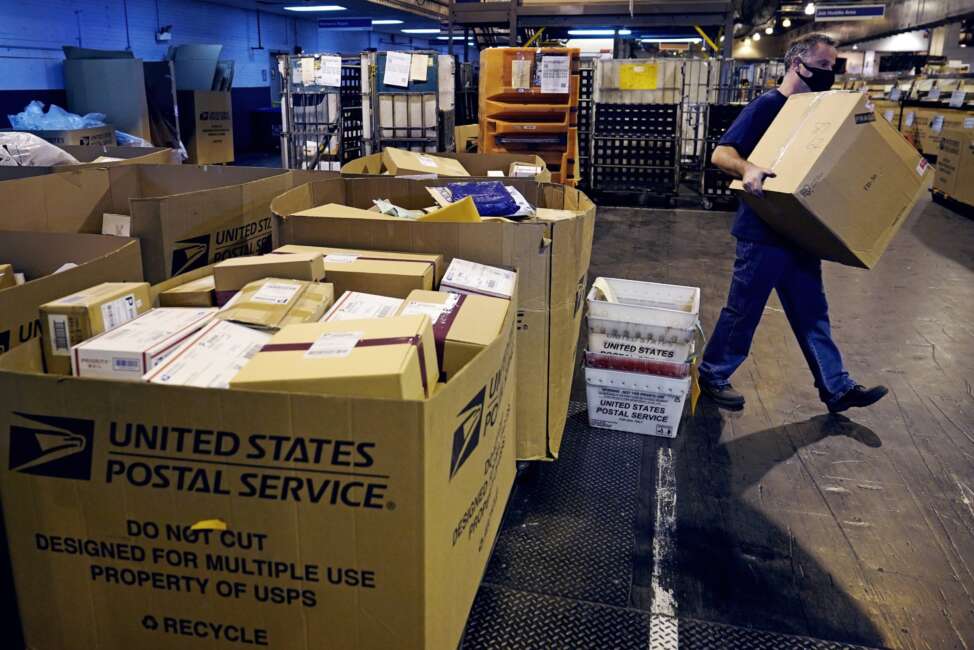 FILE - A worker carries a large parcel at the United States Postal Service sorting and processing facility Nov. 18, 2021, in Boston. Congress would lift onerous budget requirements that have helped push the Postal Service deeply into debt and would require it to continue delivering mail six days per week under bipartisan legislation that approached House approval Tuesday, Feb. 8, 2022. (AP Photo/Charles Krupa, File)