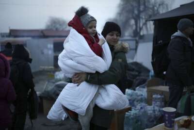 A woman walks with a child wrapped in a blanket as she waits at a refugee crossing in Medyka, Poland, Thursday, March 3, 2022. More than 1 million people have fled Ukraine following Russia's invasion in the swiftest refugee exodus in this century, the United Nations said Thursday. (AP Photo/Markus Schreiber)