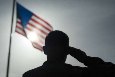 FILE - In this photo taken Aug. 26, 2019 and released by the U.S. Air Force, a U.S. Air Force Staff Sgt., salutes the flag during a ceremony signifying the change from tactical to enduring operations at Camp Simba, Manda Bay, Kenya. U.S. officials tell The Associated Press that military investigations have found that poor leadership, inadequate training and a 