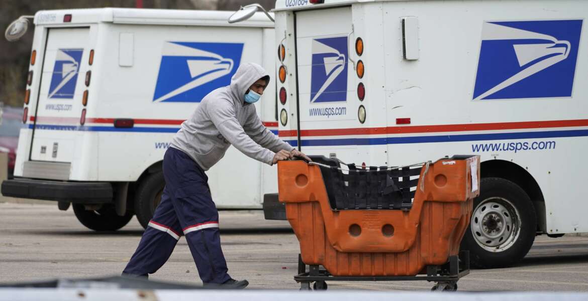 FILE - A USPS employee works outside post office in Wheeling, Ill., Dec. 3, 2021. A government watchdog said says the U.S. Postal Service's environmental evaluation used for purchases of next-generation delivery vehicles relied on some false assumptions. Jill Naamane from the Government Accountability Office told the House Oversight Committee on Tuesday that the analysis used to determine the mix of gas- and electric-vehicles overstated maintenance costs of electric vehicles and relied on gas prices that don’t reflect the current reality. (AP Photo/Nam Y. Huh, File)