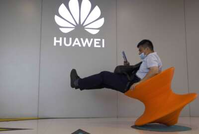 FILE - A man wearing a mask to curb the spread of the coronavirus sits near a Huawei store logo in Beijing on Friday, July 31, 2020. Chinese telecoms equipment and smartphone maker Huawei said Thursday its sales fell 14% in the last quarter from a year earlier as it pumped money into research and development while grappling with U.S. sanctions. (AP Photo/Ng Han Guan, File)