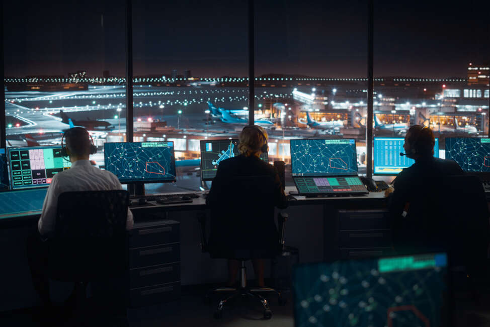 Diverse Air Traffic Control Team Working in a Modern Airport Tower at Night. Office Room is Full of Desktop Computer Displays with Navigation Screens, Airplane Flight Radar Data for Controllers.