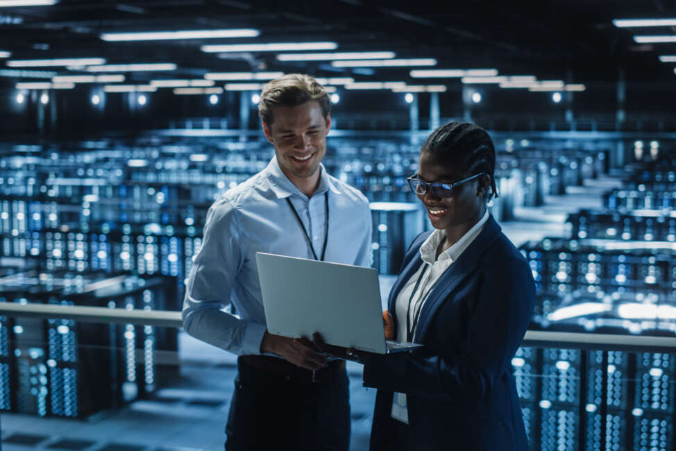 Data Center Female System Administrator and Male IT Specialist talk, Use Laptop. Information Technology Engineers work on Cyber Security Protection in Cloud Computing Server Farm.