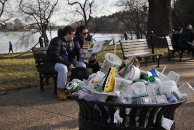 FILE - A trash can overflows as people sit outside of the Martin Luther King Jr. Memorial by the Tidal Basin, Dec. 27, 2018, in Washington, during a partial government shutdown. The Interior Department said Wednesday, June 8, 2022, it will phase out single-use plastic products on national parks and other public lands over the next decade, targeting a leading source of U.S. plastic waste such as food and beverage containers, straws and bags.(AP Photo/Jacquelyn Martin, File)