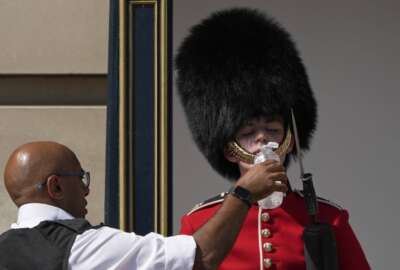 A police officer givers water to a British soldier wearing a traditional bearskin hat, on guard duty outside Buckingham Palace, during hot weather in London, Monday, July 18, 2022. The British government have issued their first-ever 