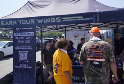 Racing fans stop at the U.S. Air Force recruiting tent prior to a NASCAR race at the New Hampshire Motor Speedway, Sunday, July 17, 2022, in Loudon, N.H. These are tough times for military recruiters.  All services are having problems finding young people who want to join and can meet the physical, mental and moral requirements.  Recruiters are offering bigger bonuses and other incentives to those who sign up. And they are seizing on the boost that Hollywood may offer – such as the buzz over Top Gun. (AP Photo/Charles Krupa)