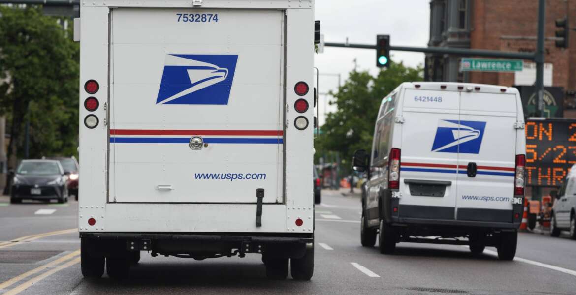 FILE - A USPS logo adorns the back doors of United States Postal Service delivery vehicles as they proceed westbound along 20th Street from Stout Street and the main post office in downtown Denver, Wednesday, June 1, 2022. USPS plans to substantially increase the number of electric-powered vehicles it’s buying to replace its fleet of aging delivery trucks, officials said Wednesday, July 20, 2022. (AP Photo/David Zalubowski, File)