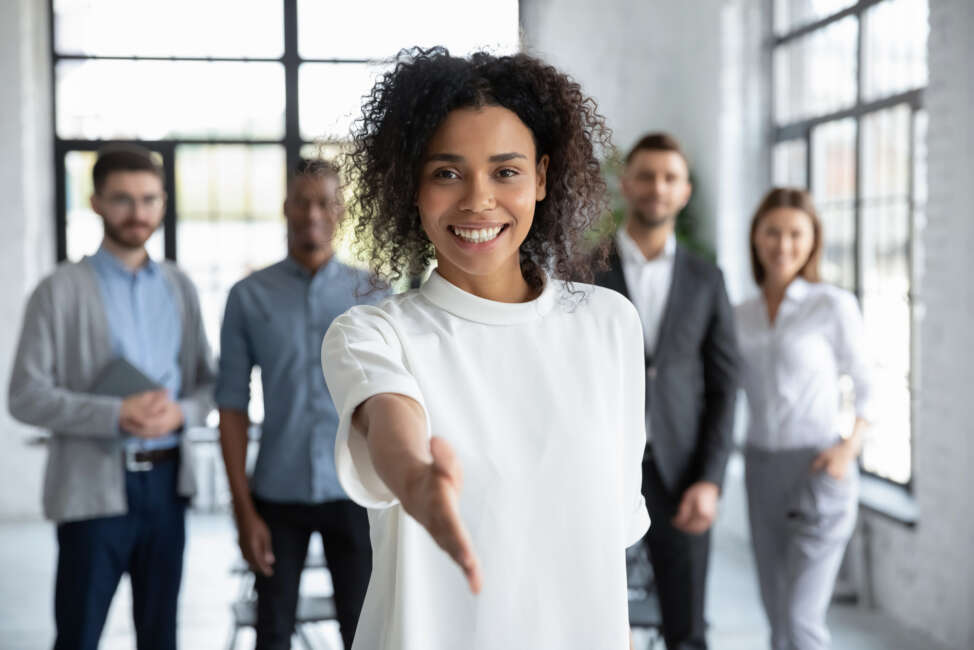 Head shot portrait smiling African American businesswoman offering handshake, standing with extended hand in modern office, friendly hr manager or team leader greeting or welcoming new worker